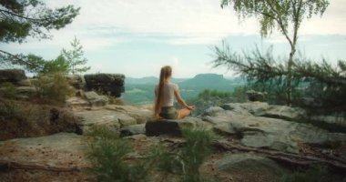 Ağaçlarla çevrili ve Bastei, Sakson İsviçre 'nin engin manzarasına bakan kayalık bir uçurumda meditasyon yapan bir kadın...