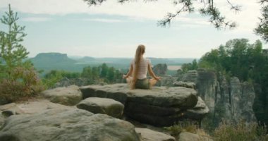 Almanya 'da Bastei' nin güzel manzarasını seyreden ve meditasyon yapan bir kayanın üzerinde bağdaş kurmuş bir kadın oturuyor...