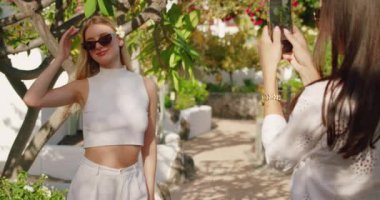 Güneş gözlüklü ve saçında çiçekle poz veren bir kadın, bahçede dikilmiş, fotoğraf çekiliyor...