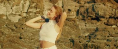 Kadın dışarıda saçlarını tararken, kayalık bir zemine yaslanırken, sıcak güneş ışığında yıkanırken, bir anın tadını çıkarıyor...