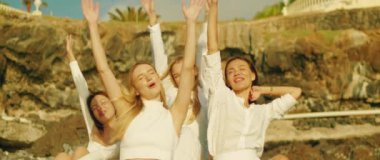 Dört kadın sevinçle kollarını havaya kaldırır. Güneşli bir günde, açık havada, kayalık bir arazinin yanında gülümserken...