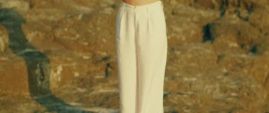 Beyaz ekin bluzlu bir kadın saçını dışarıda tararken güneşli bir anın tadını çıkarıyor. Kayalık bir yüzeyde pantolon giyen kadın vücudunun yakın çekimi...