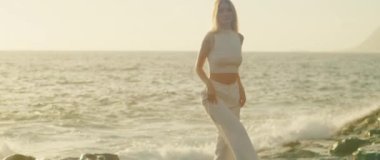 Kadın, kıyıda yürürken kameraya gülümsüyor. Okyanus dalgaları yavaşça arkasına çarpıyor. Los Gigantes Tenerife, İspanya 'da...