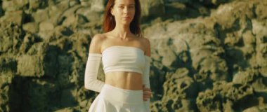 Beyaz omuzlu bir kadın gün ışığında kayalık kayalıkların önünde duruyor..