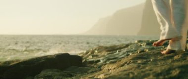 Gün batımında okyanus dalgaları yakınındaki engebeli kayaların üzerinde ayaklar barışçıl bir doğal atmosfer yaratıyor..