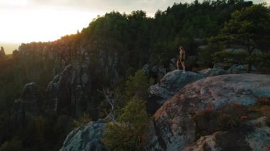 Yürüyüşçü kadın Schrammsteine Elbe Kum Taşı Dağları 'ndaki kayalık bir çıkıntının tepesinde gün batımını seyrediyor..