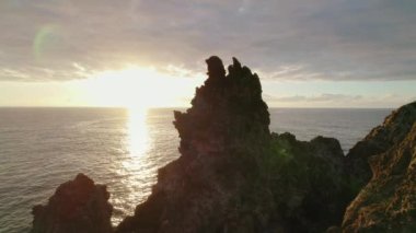 Karanlık engebeli uçurumları ve gün batımında sonsuz okyanus manzarası olan dağlık bir arazi...