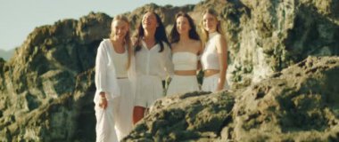 Güneşin altında kayalık bir çıkıntıda dururken birlikte gülen ve gülen dört kadın..