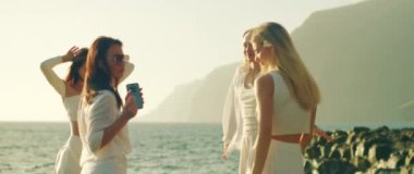 Rahat beyaz elbiseli kadınlar, sahilin kıyısında, manzaralı uçurumlarda ve okyanusta nefes kesici bir zemin oluşturan neşeli bir dansı paylaşıyorlar.