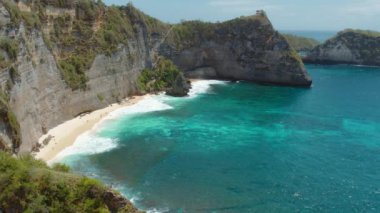 Nusa Penida Adası Bali 'deki turkuvaz suları ve beyaz kumlu uçurumlar boyunca gizli bir kumsalın insansız hava aracı görüntüleri..