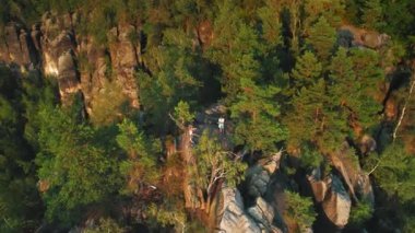 Yoğun yeşil orman ağaçlarıyla çevrili kayalık bir uçurumda iki insanın hava görüntüsü. Bir kayanın üzerinde duran yürüyüşçüler, doğanın ve keşiflerin özünü yakalıyorlar...