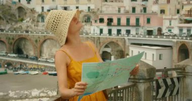Kadın elinde haritayla Atrani şehrinin plajına ve tarihi mimarisine bakıyor..