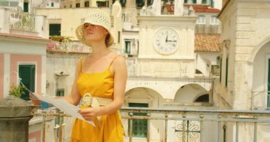 İtalya 'nın Amalfi kıyısındaki Atrani şehir merkezinde tarihi saat kulesi ve pastel binaların yanında elinde harita tutan kadın..