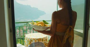 Bir kadın yaz günü İtalya 'nın sahil kesimindeki terasa bir kase limon taşır..