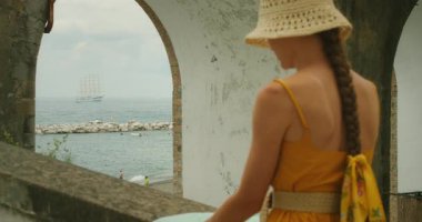 Atrani şehrinde geniş bir kemerden denize bakan bir kadın..