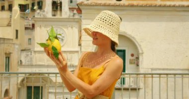 Tarihi şehir saatinin önünde limon tutan kadın ve İtalya 'nın Atrani şehrinde binalar..