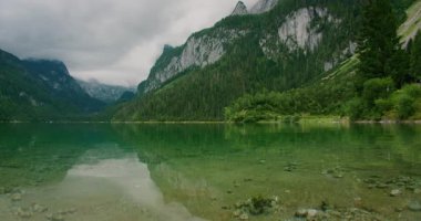 Kristal berrak dağ gölü Gosausee bulutlu gökyüzünün altındaki tepeleri yansıtıyor.