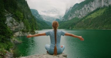 Kadın bir dağ gölünde bağdaş kurup elleriyle kalp şeklinde oturuyor..