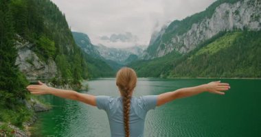 Canlı, yeşil bir göle bakan bir kadın önünde dağlar kadar geniş bir alanı kucaklıyor. Doğayla benlik arasındaki uyum, vahşi doğanın kalbinde sakin bir an...