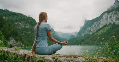 Huzurlu göl kenarında huzur içinde meditasyon yapan bir kadın. Arka planda Avusturya manzaralı bir dağ manzarası var..