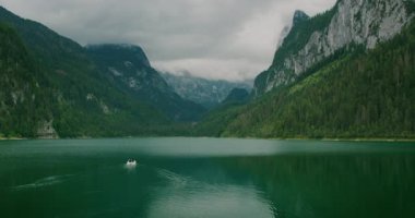 Turistli küçük bir tekne Avusturya 'da dağlarla ve sisle çevrili derin yeşil bir göl boyunca ilerliyor..