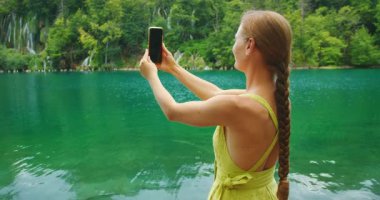 Uzun örgülü kadın yaz seyahati sırasında Plitvice Ulusal Parkı 'nda yeşil gölün kenarında selfie çekiyor..
