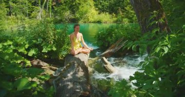 Yeşillik Plitvice Hırvatistan ormanında, devrilmiş bir ağacın üzerinde meditasyon yapan kadın.