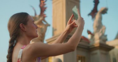 Tarihi bir Avrupa anıtının dekoratif heykellerinin önünde akıllı telefon fotoğrafı çeken bir kadın..