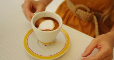 Süt köpüklü bir fincan espresso bir kadının İtalya 'da kahvenin tadını çıkarırken bir fincan çay tabağının üzerinde oturur..