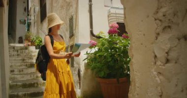 Kadın, Atrani şehrindeki pitoresk bir sokakta saksı çiçeklerinin yanında harita okumak için duruyor..