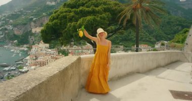 Gülümseyen kadın yaz günü Amalfi sahili terasında büyük bir limon tutuyor..
