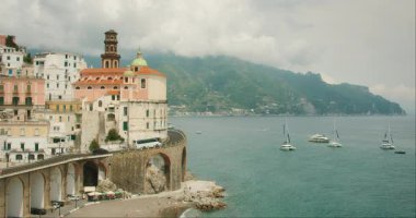 Arka planda tekneler ve dağlar olan Atrani kıyı köyünün manzarası..
