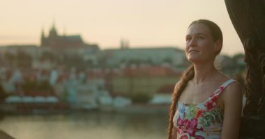 Gülümseyen kadın, altın bir günbatımında tarihi Prag şehri manzarasına bakan Charles Köprüsü 'nde duruyor..