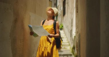 İtalya 'nın Atrani şehrinin arka sokağında elinde haritayla binalara bakan bir kadın..