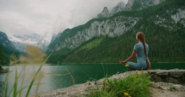 Kadın, sakin bir göle bakan kayalık bir çıkıntıda meditasyon yapar ve yüksek tepelere çıkar..