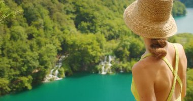 Hasır şapkalı kadın yaz güneşli bir günde Plitvice Gölleri 'ndeki şelalelere bakar..
