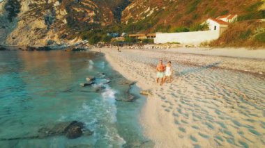 Çift sıcak bir akşamda Petani Sahili boyunca yürür. Dalgalar yavaşça Kefalonia 'daki kuma dokunur..