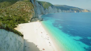 Yaz mevsiminde Yunanistan 'ın turkuaz sularıyla tenha beyaz kumsalın üzerindeki bir uçurumda duran kadın.