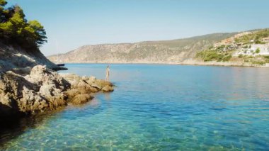 Asos köyü Kefalonia 'da kayaların üzerinde duran kadın, Yunanistan' ın sakin denizine bakıyor.