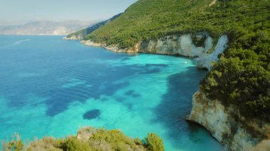 Paxos Adası 'nın kayalıklarında duran çift turkuaz sularla çevrili ve berrak gökyüzünün altında yemyeşil tepeler..