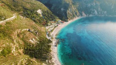 Petani plajı yeşil bir yamacın yanında şemsiyelerle ve Kefalonia 'da gök mavisi suyla kaplı..
