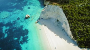 Kayalıkların eteklerinde beyaz çakıl taşı plajı. İnsanlar dinleniyor ve tekneler Kefalonia 'da Yunanistan' a yakın..