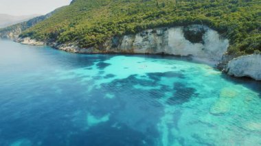 Turkuaz Kefalonya 'da yaz aylarında bir teknenin yanında kayalıkları ve yemyeşil ormanı olan bir koy..