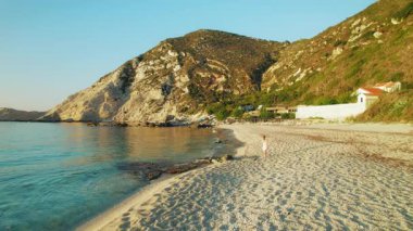 Yunanistan 'ın Kefalonia kentindeki kayalık tepelerin yanından tek bir kişinin geçtiği yaz plajı.