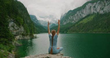 Gosau Gölü 'ne bakan bir kayanın üstünde yoga yapan kadın elleriyle kalp oluşturuyor..