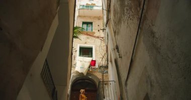 Amalfi kıyısındaki eski bir İtalyan kasabasındaki dar bir sokakta yosunlu merdivenlerden inen bir kadın. Çamaşırlar balkonlarda asılı...