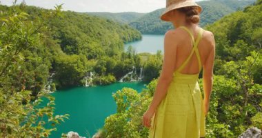 Plitvice Şelalesi 'ne ve yemyeşil tepeden göle bakan genç bir kadın..