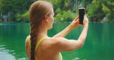 Yaz tatilinde Plitvice Lakes Ulusal Parkı 'nda yeşil göl kenarında fotoğraf çeken bir kadın..