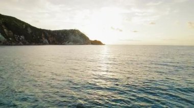 Sakin denizin üzerinde gün batımı ufukta engebeli uçurumlar.