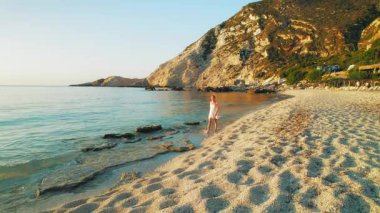 Kefalonia 'da gün batımında sahilde yürüyen beyaz elbiseli genç bir kadın..
